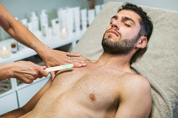 Serene guy getting wax hair removal from chest in salon